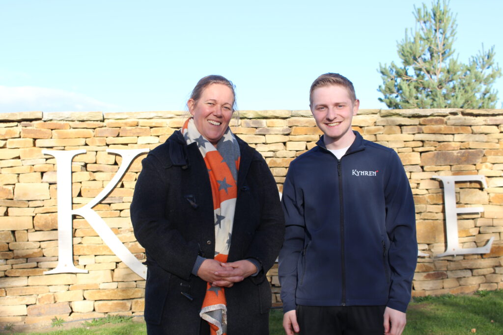 Anna Warnecke, CEO of Kynren, with Jaden Dixon, Kynren's Visitor Operations Manager, smile to the camera in front a stone Kynren sign.