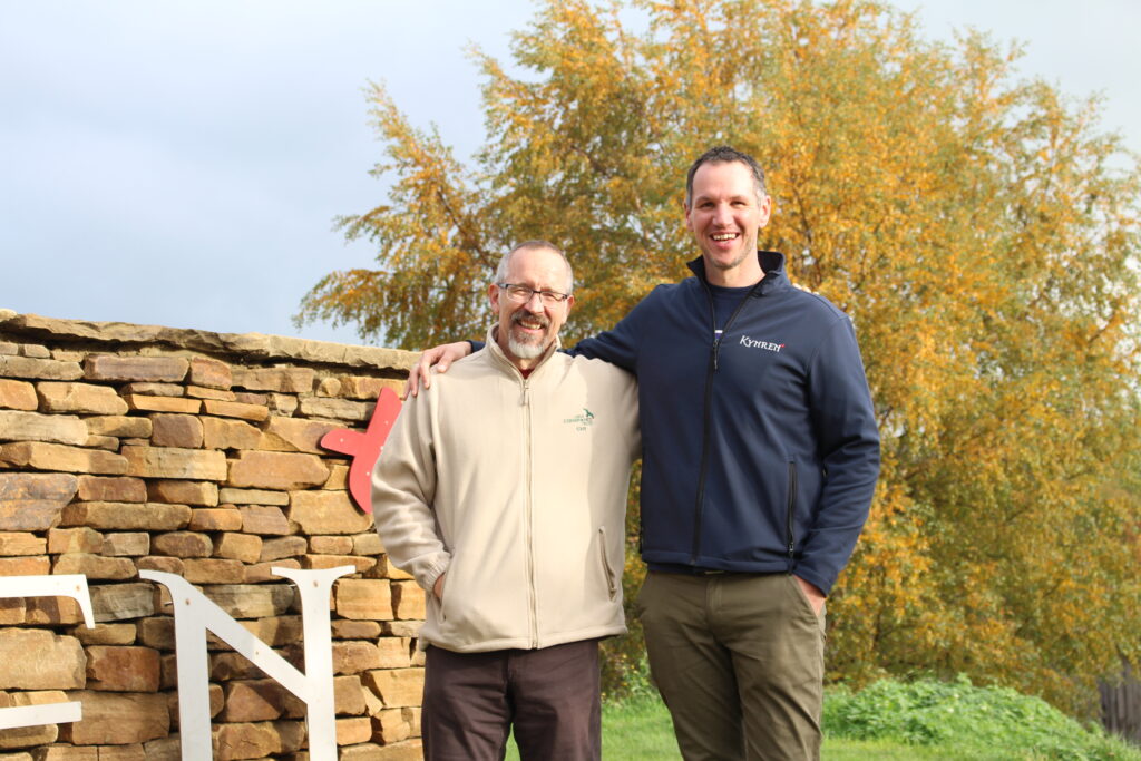 two men stand in front of a stone sign