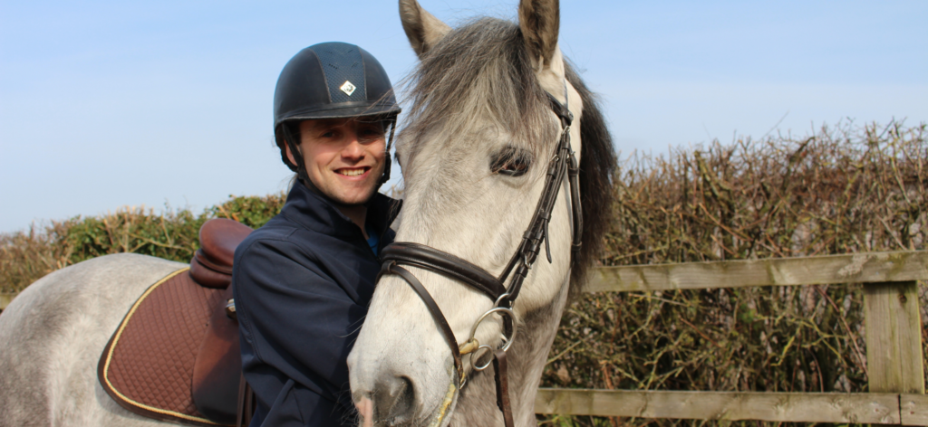 A man smiles at the camera while a horse's head hugs his body