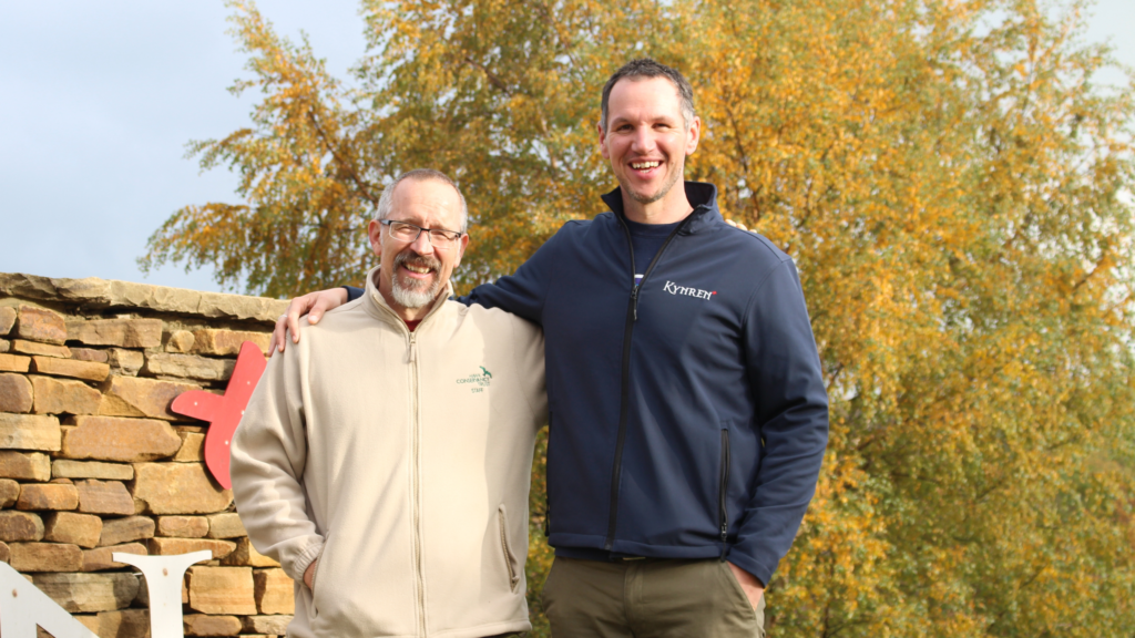two men stand in front of a stone sign outside