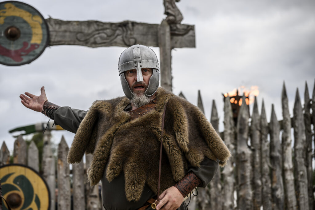 A viking beckons towards the entrance of a settlement