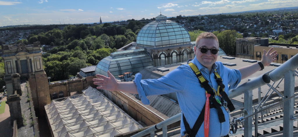 a man in sunglasses and climbing harnesses stands on top of a palace rooftop
