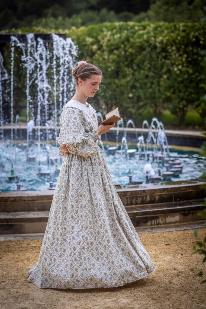 a woman reads a book in front of a decorative fountain in a hedgemaze