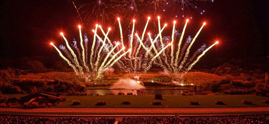 fireworks above a huge outdoor stage, fit with a lake