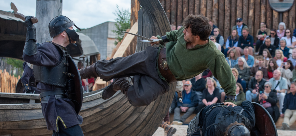 three vikings fight in Kynren's Land of the Vikings. One man kicks another in the chest, while using the third as a prop to do so.